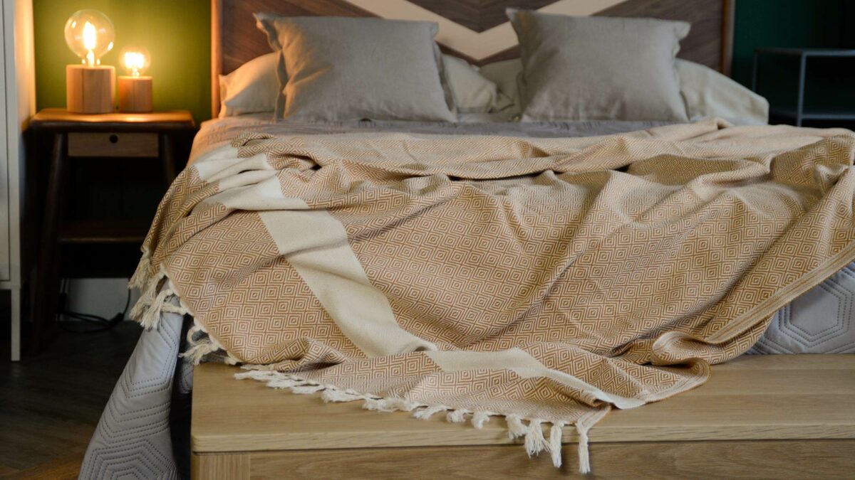 woven cotton blanket in cream and orange shown draped over Hoxton bed