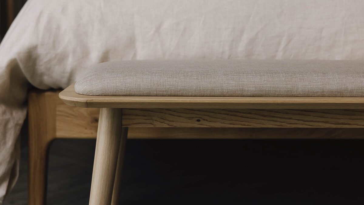 closeup of padded bench with oak base at the foot of a bed.