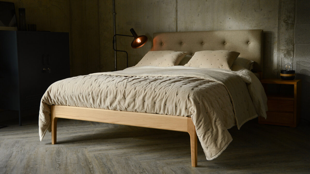 A wool upholstered headboard and oak framed Bloomsbury bed with pale beige velvet quilt and cushions