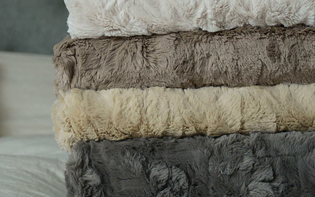 softest faux fur throws in a range of neutral grey and stone colours shown in a stack