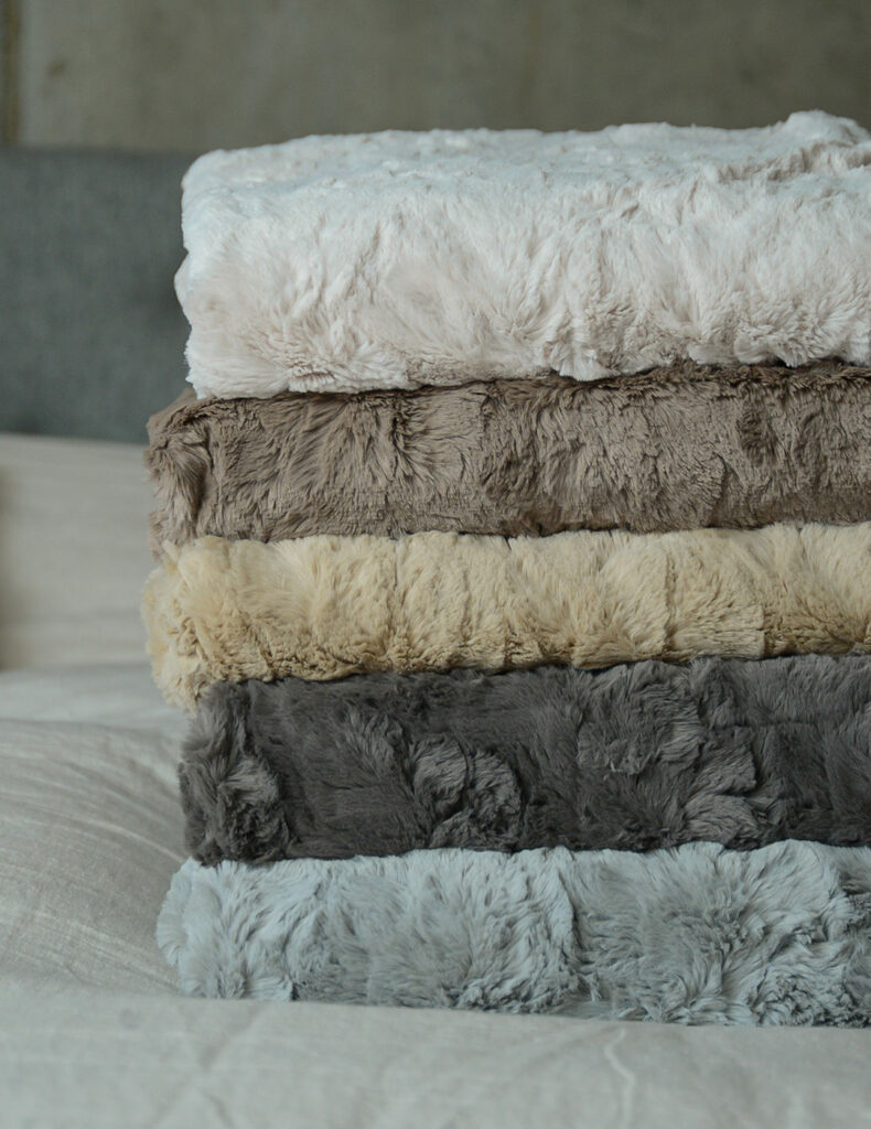 softest faux fur throws in a range of neutral grey and stone colours shown in a stack