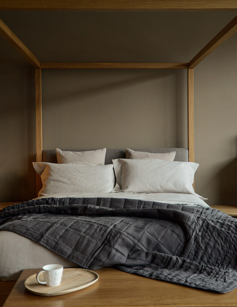 linen quilted ruffle edge throw in Charcoal shown draped on a wooden framed 4 poster bed