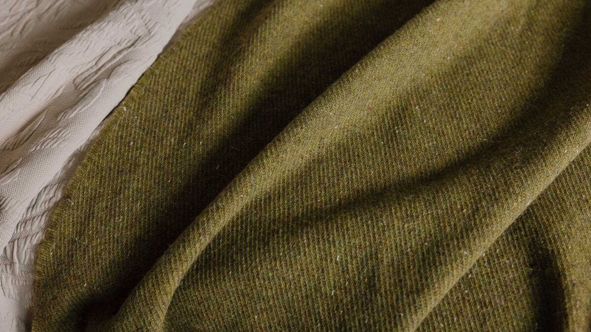 Close up of a recycled merino lambswool throw in olive green.