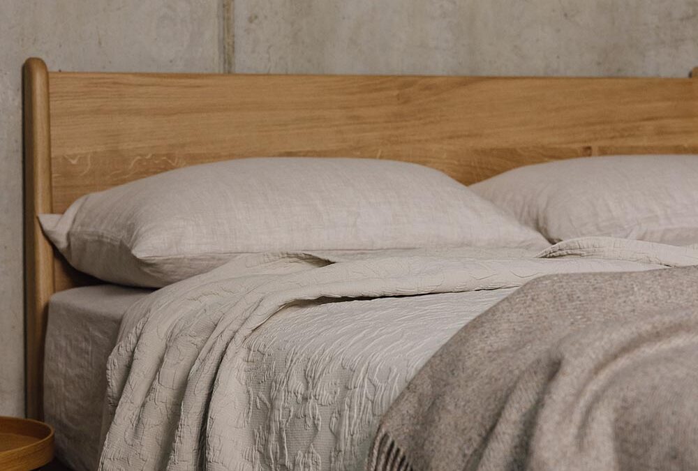 Portrait shot of an oak bed with beige linen and a griege woollen throw.