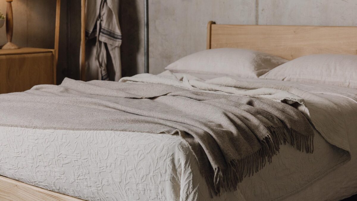 Greige throw draped over ecru bedding on an English Oak Bed.