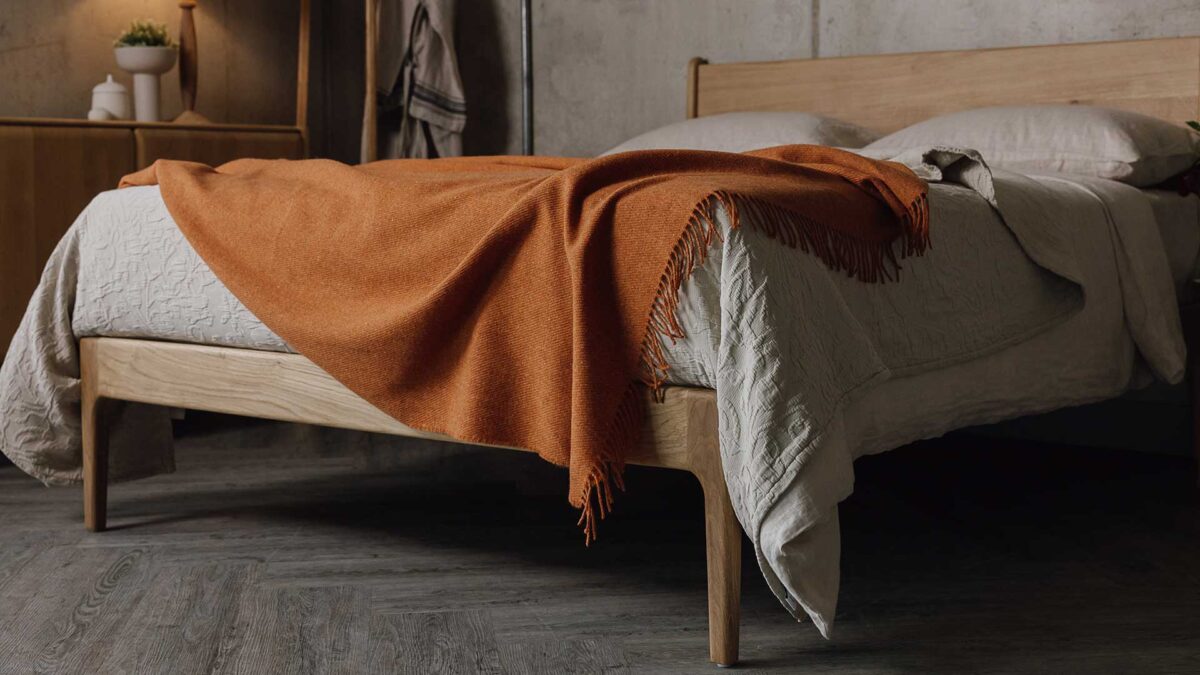 3/4 view of the bottom of a bed with stone linen and a burnt orange throw.