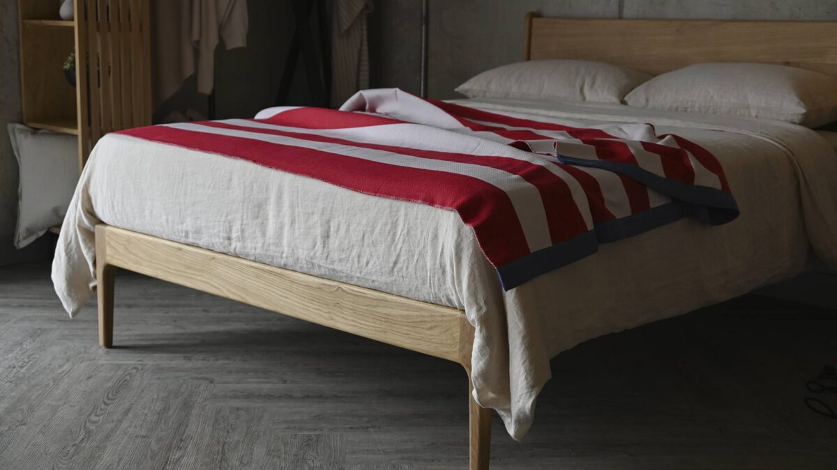 Red and ivory striped throw with dark blue edge draped over a bed with stone bed linen.
