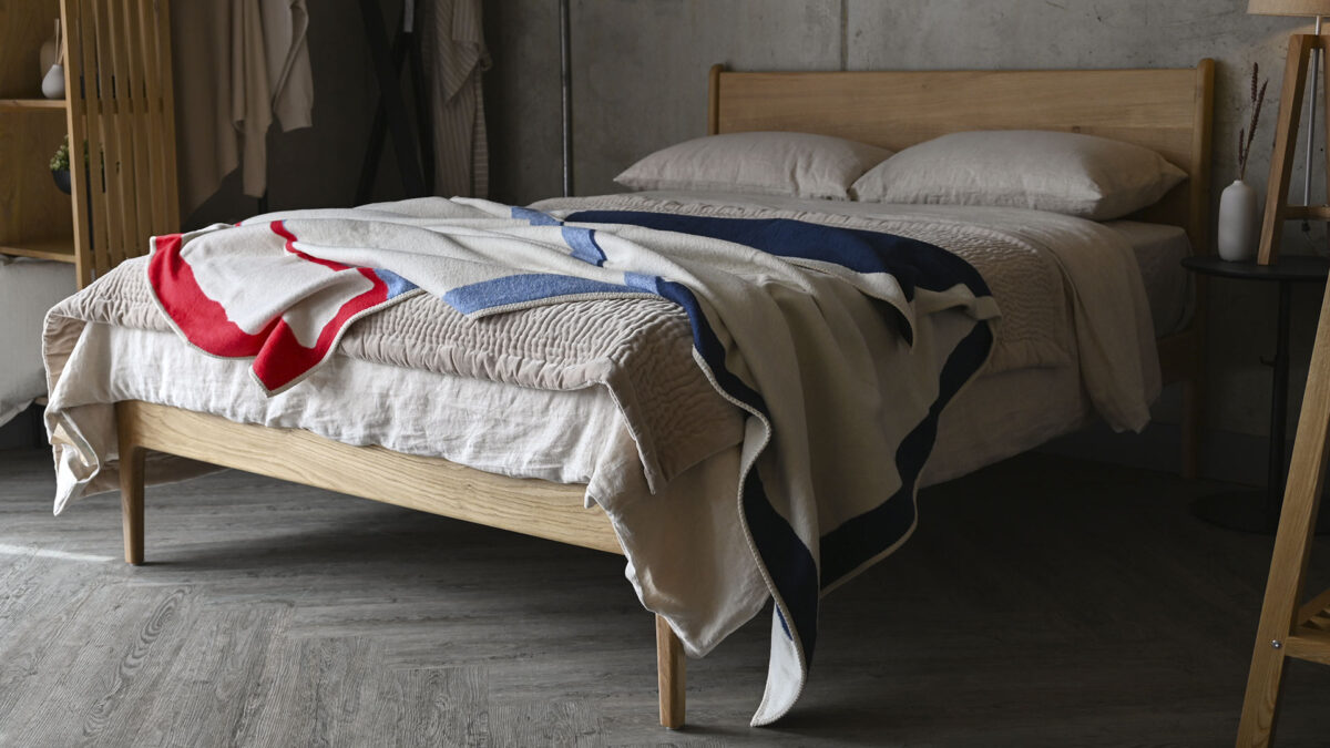 Oak bed frame with stone pillows and duvet cover, a modern abstract throw in ivory, red and blue messily thrown over the top.