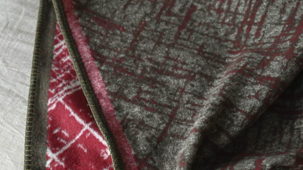 Red throw with white crosshatch pattern and olive green border. Stitching detail around the edge.