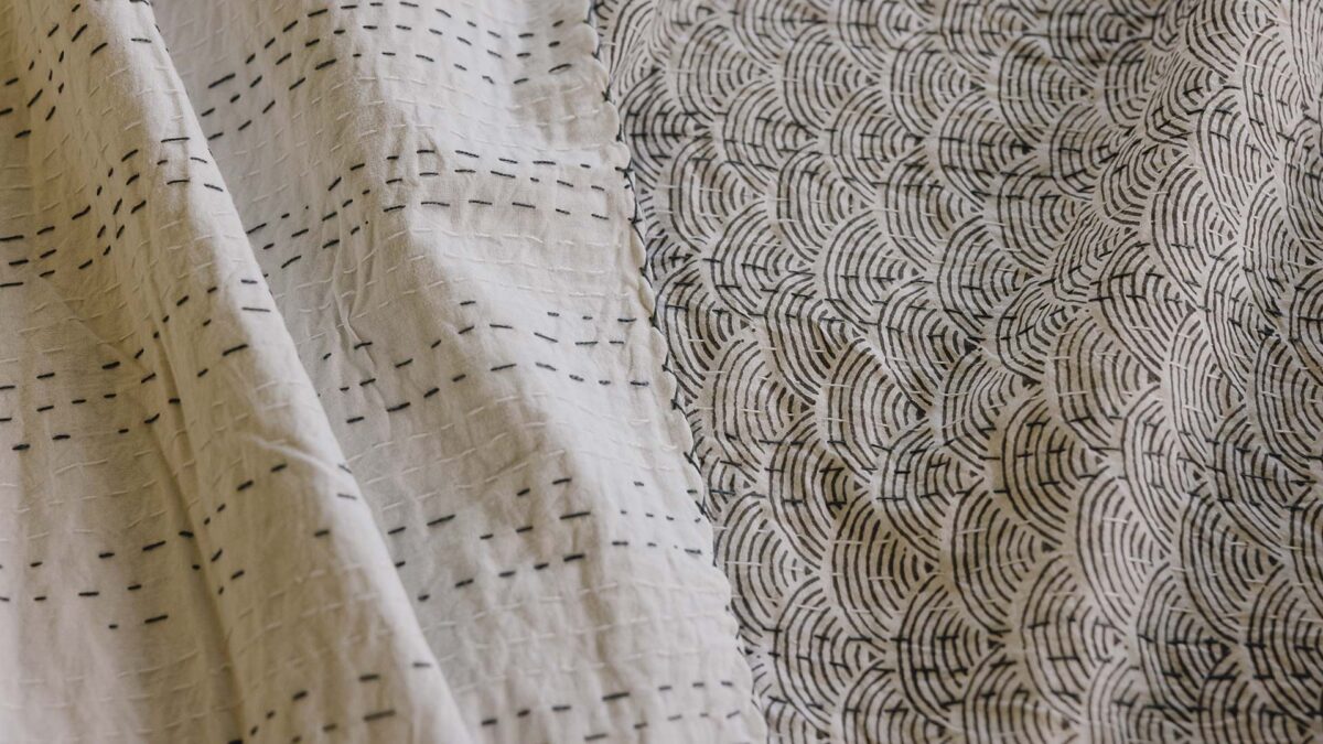 closeup of a reversible grey bedspread, folded over so that both front (wave print) and back (stitching detail) are visible.
