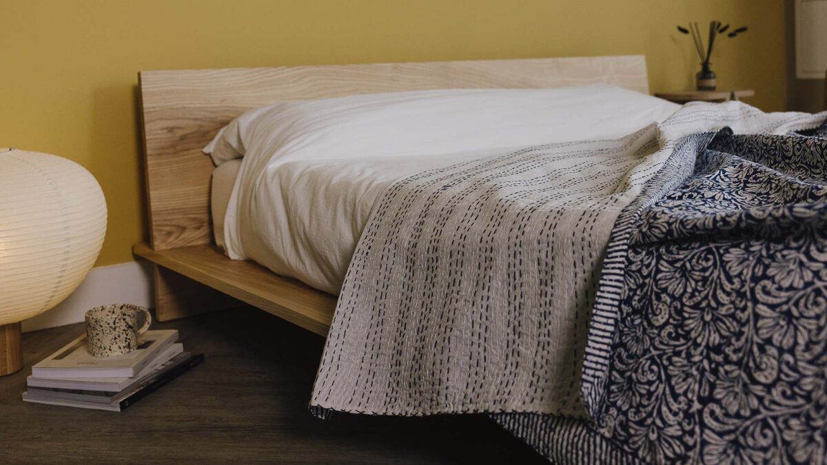 Blue floral bedspread messily draped across white bedding. Top folded down to show white reverse with blue stitching detail.