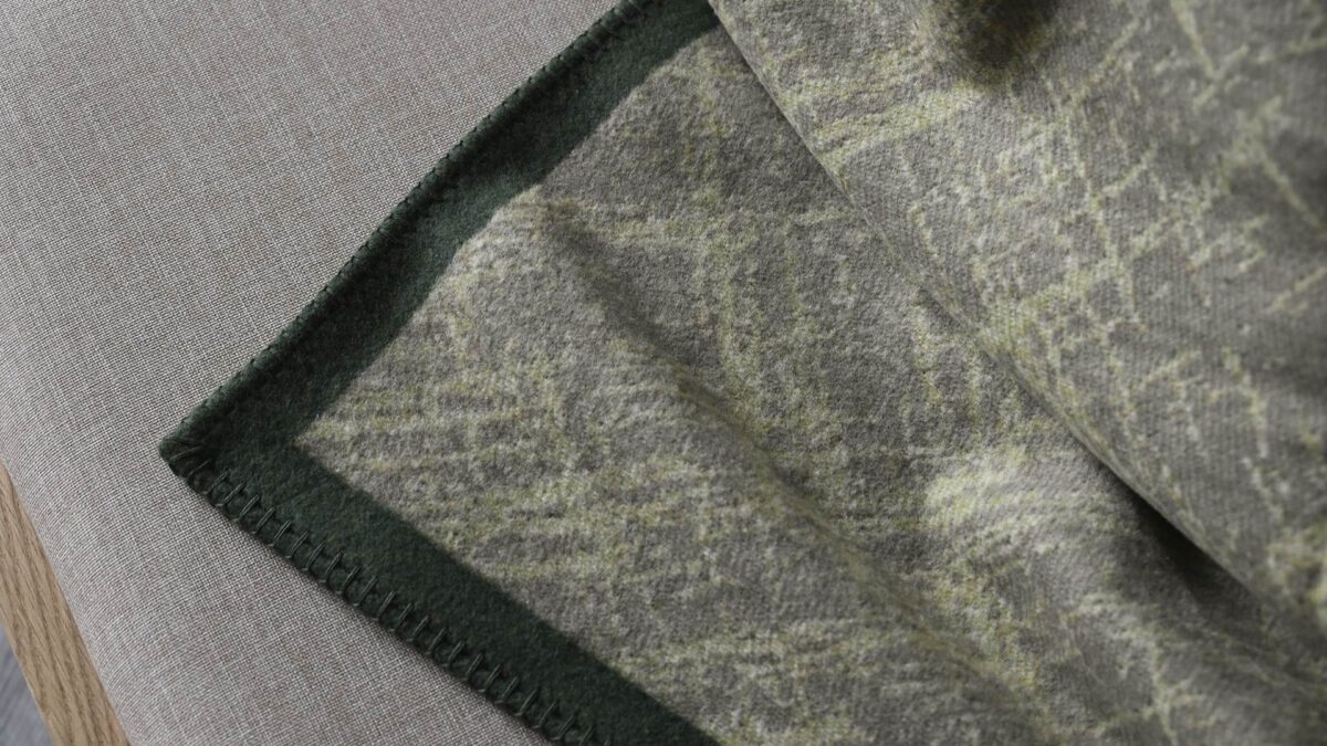 Sage green throw with bright crosshatch pattern and dark green border. Stitching detail around edge.