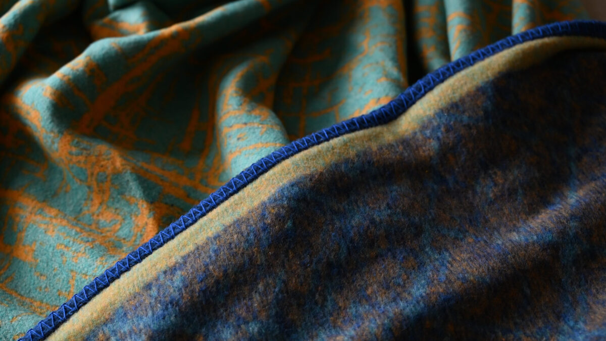 reversible throw, folded to show both sides; aqua with yellow crosshatch pattern and deep blue.
