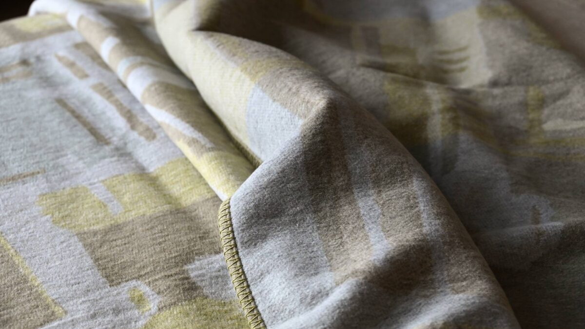 close up of a sage green and taupe throw with an abstract pattern.