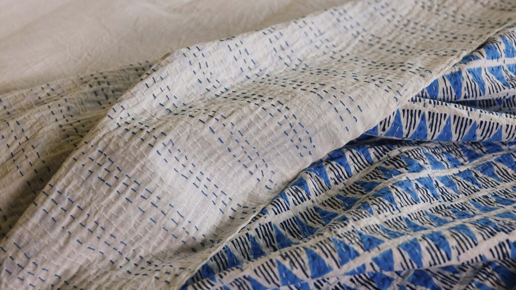 Reversible block print bedspread with blue triangle pattern on one side and blue and white stitch detailing on a white background on the reverse.
