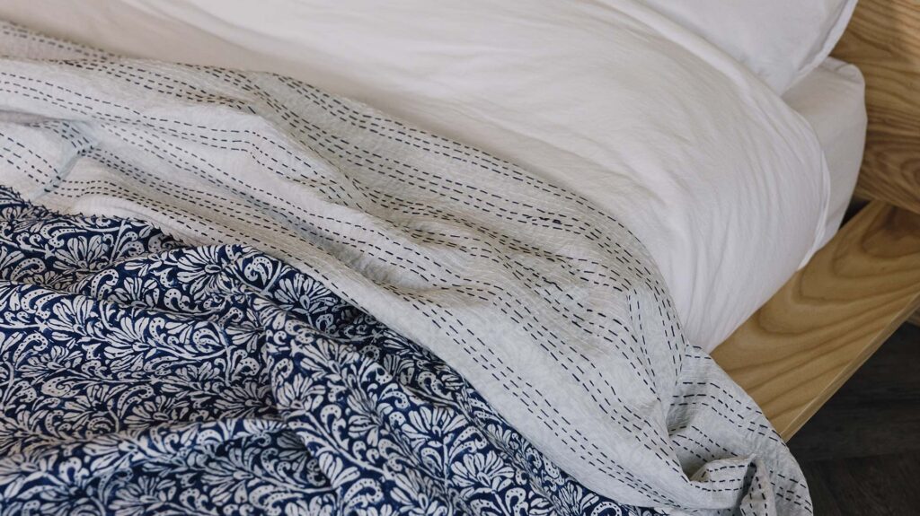 Closeup of blue floral kantha bedspread with the top folded down to show the reverse - striped pattern blue stitching on white material.