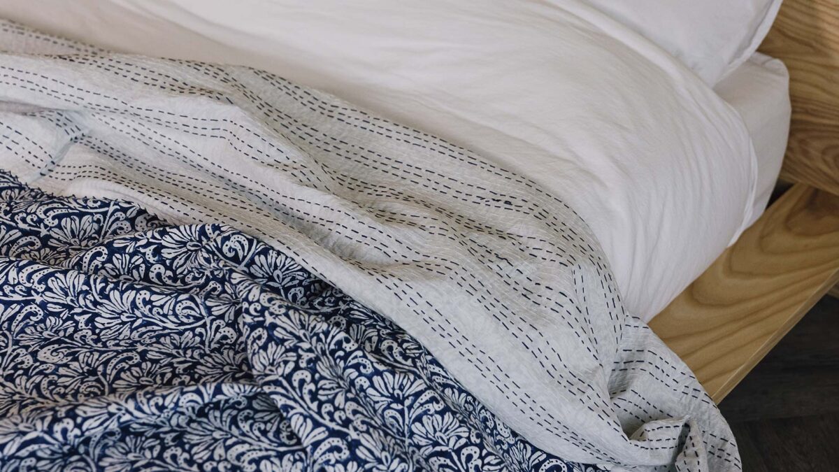 Closeup of blue floral kantha bedspread with the top folded down to show the reverse - striped pattern blue stitching on white material.