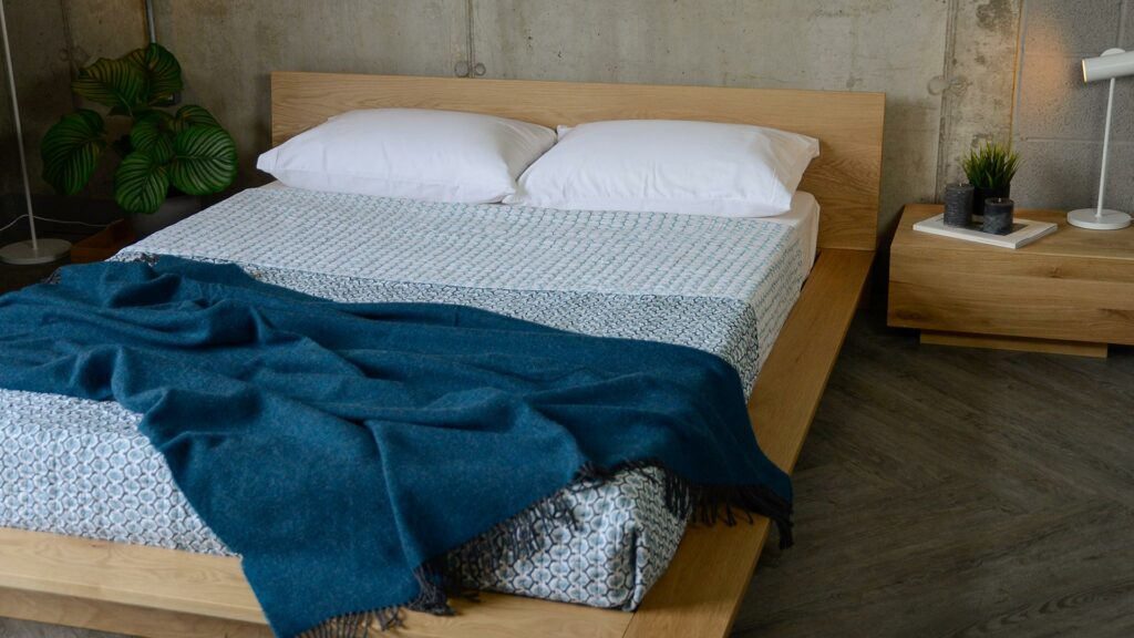 blue and white quilted bedspread shown with a blue wool throw and on a low oak oregon bed