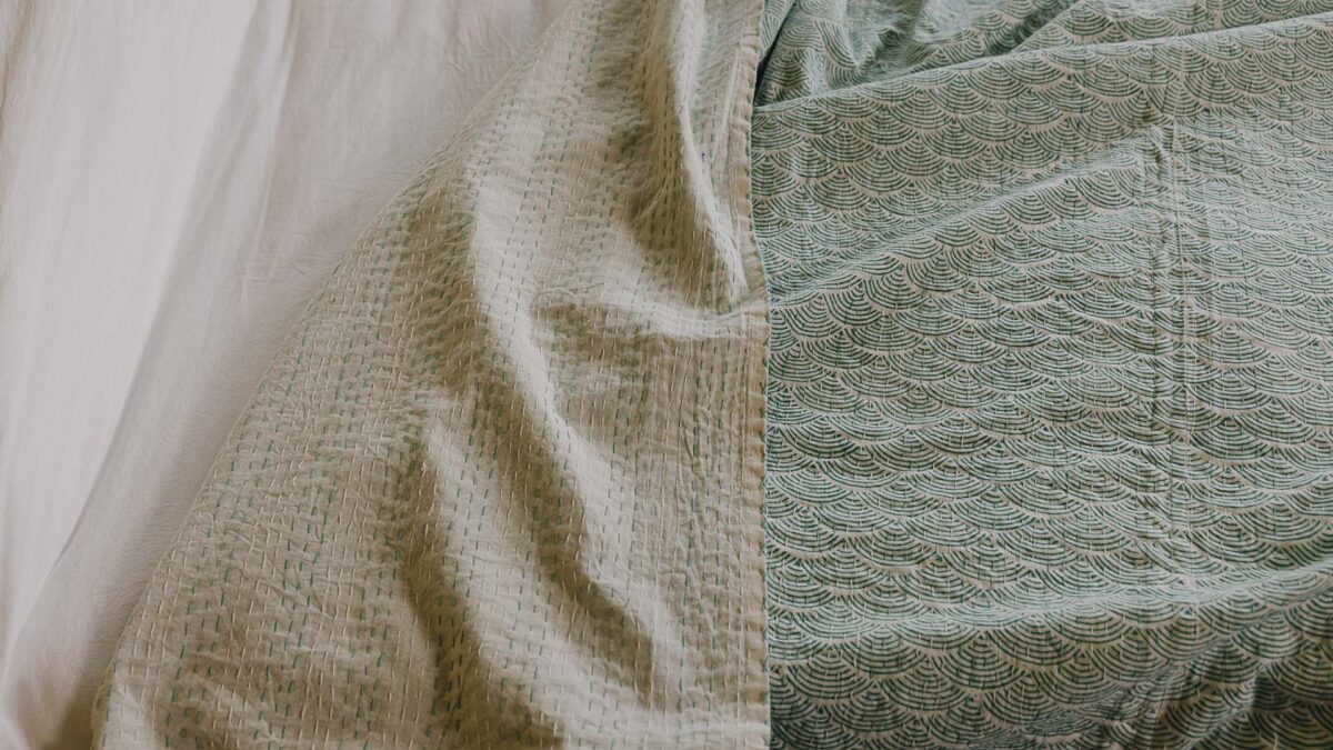 Closeup image of green kantha bedspread with wave pattern. The hand-stitched reverse is also visible to the left of the image.