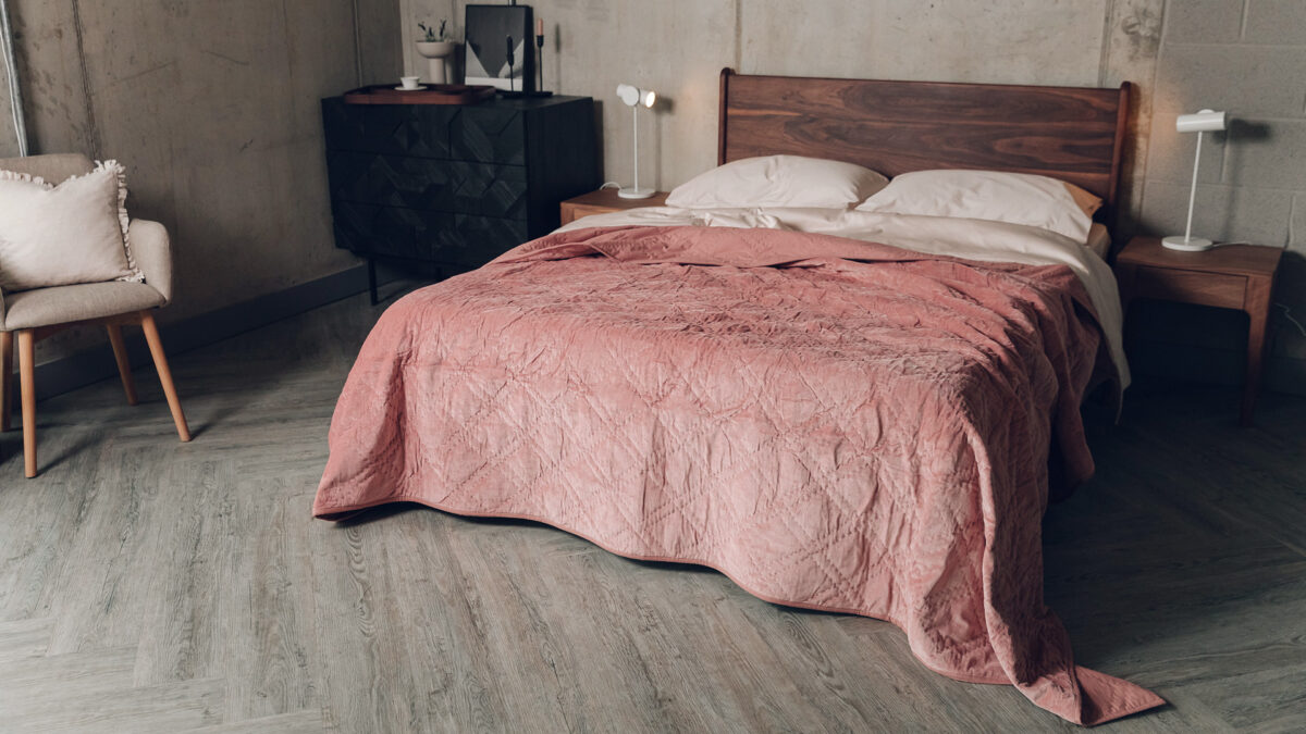 dusky rose coloured quilted velvet bedspread shown on a kingsize wooden bed