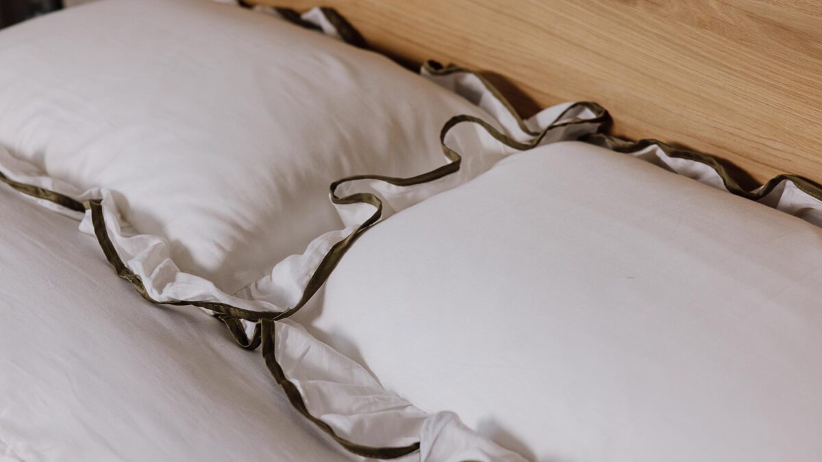 A close up image of two pillows dressed with the white bedding with a green ruffled border.