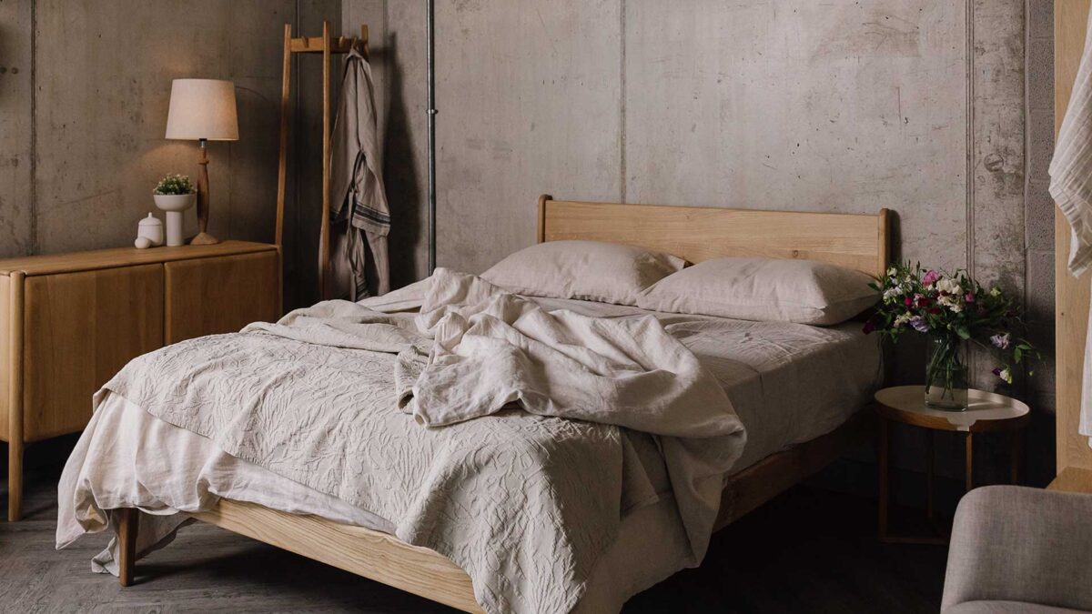 Bedroom scene with oak side board and coat stand. English oak bed frame centre of shot, with rumpled ecru bedding and throw.