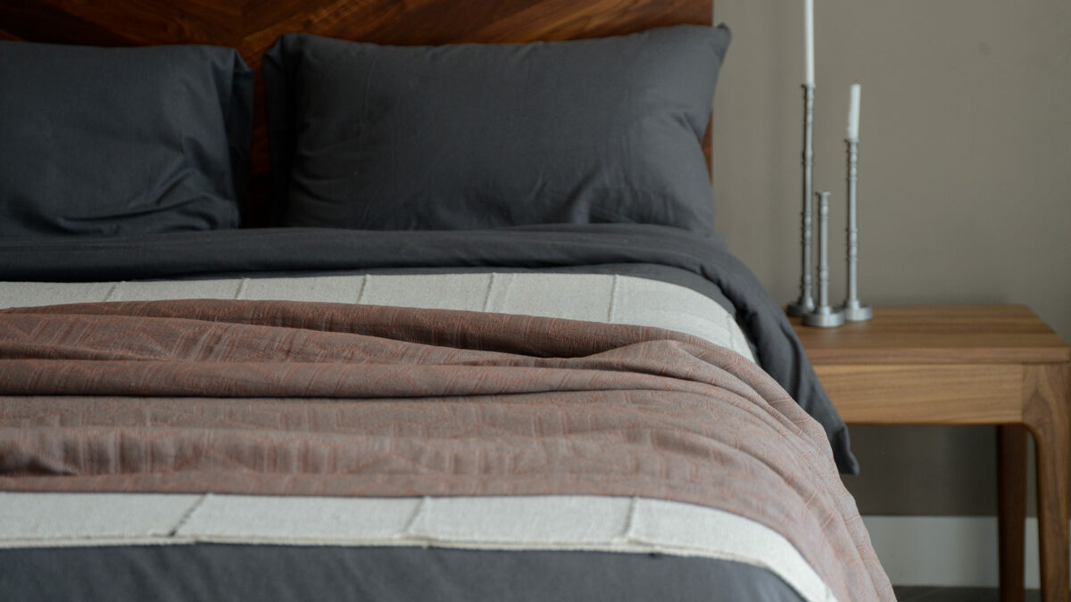 textured pattern lightweight bedspread in a rust red colour shown with dark grey bedding