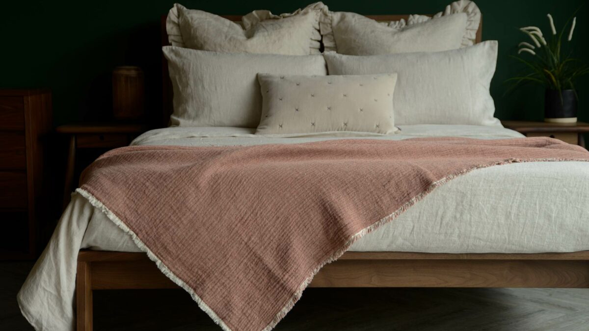 organic cotton reversible throw in blush pink and ivory shown on a kingsize bed