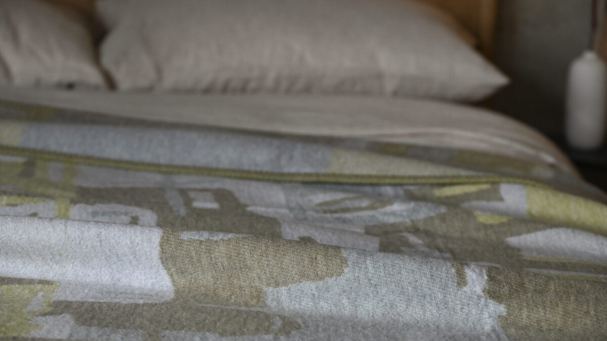 close up of a sage green and taupe throw with an abstract pattern.