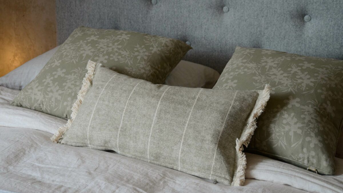 a collection of sage green and taupe cushions displayed on a bed