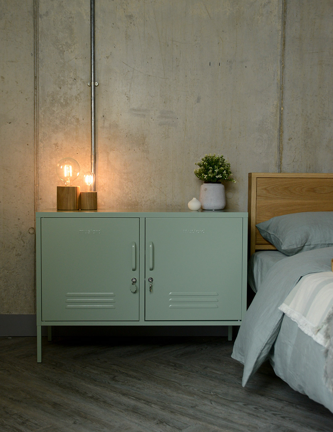 locker style storage cabinet in sage green used as a bedside table