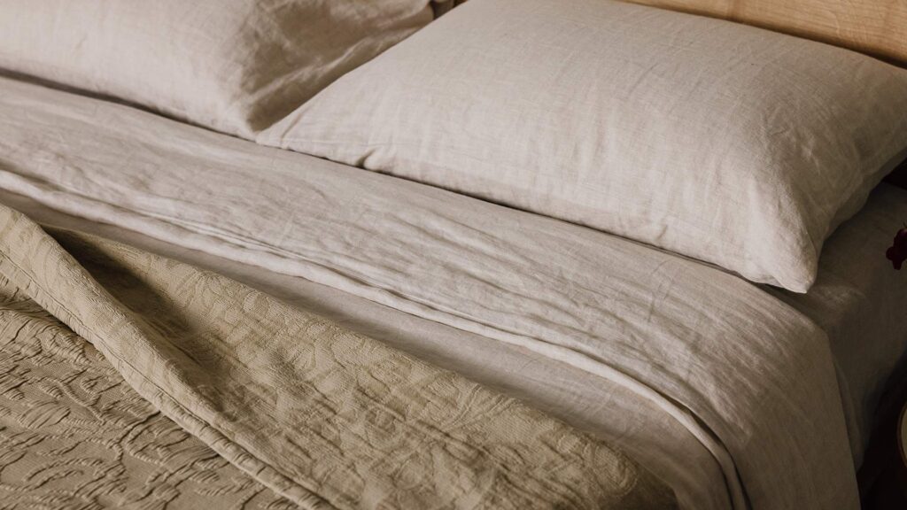 Close up shot of the organic linen bedding in ecru with the floral textured bedspread in sand on top.
