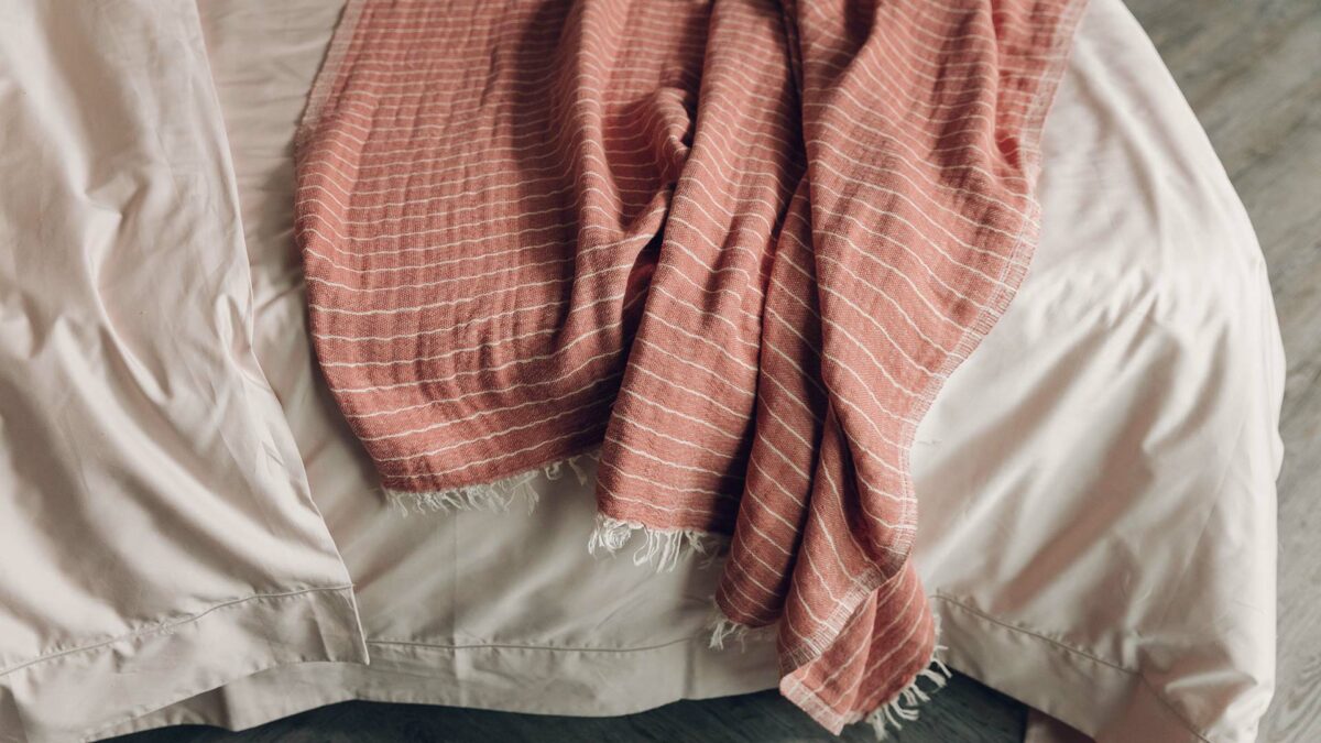 shell coloured cotton bedding shown with a striped terracotta throw