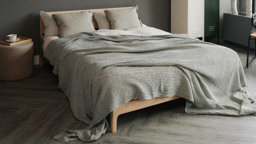 A bedroom setting with a silver green large bed throw