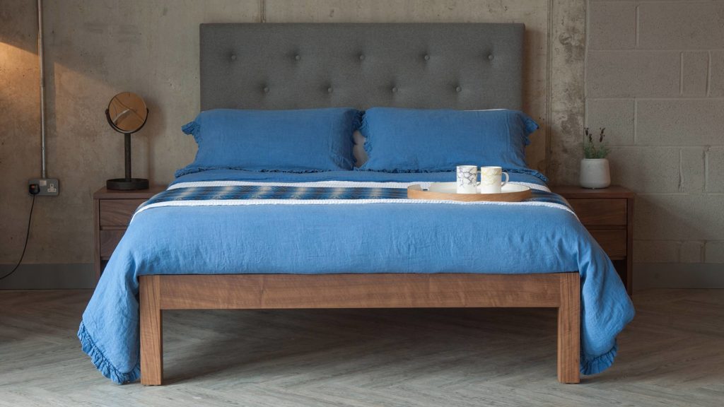 Classic British made Skye wooden bed with tall upholstered headboard and dressed in blue linen bedding