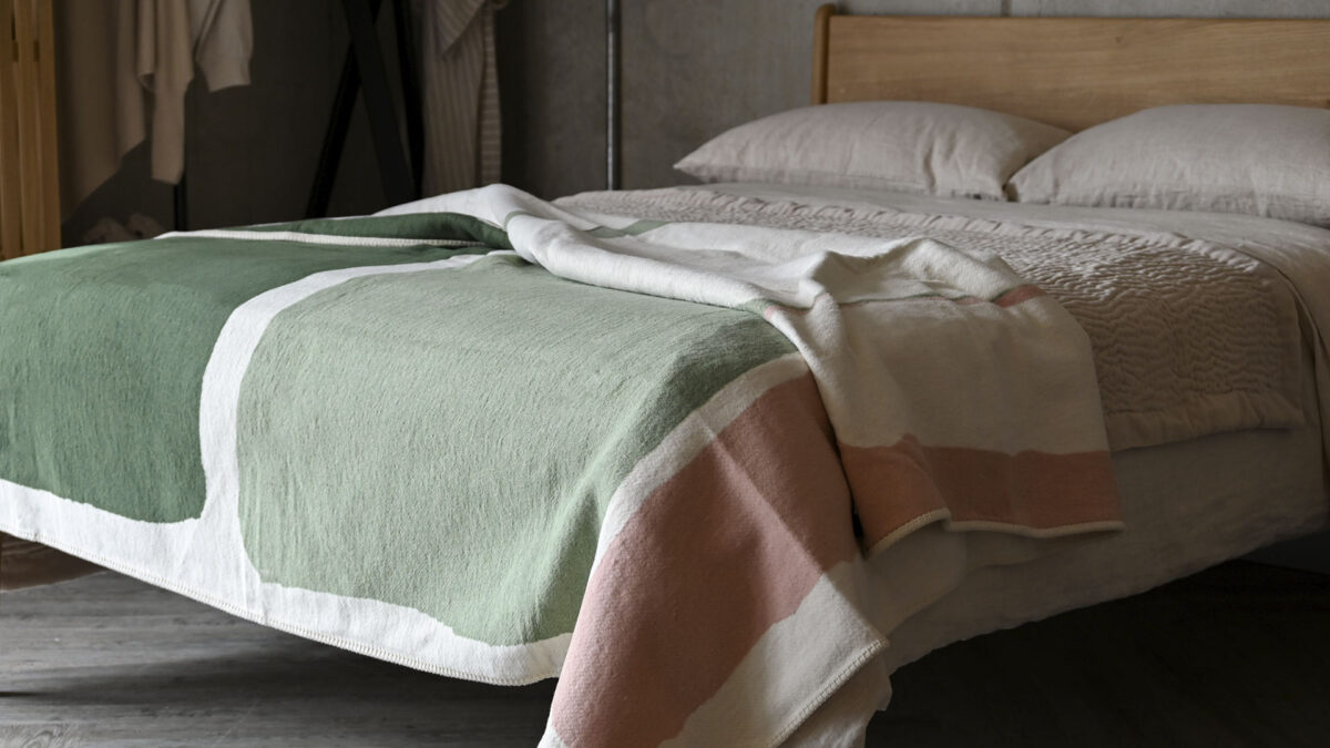 throw with green, Ivory and blush abstract blocks photographed draped across the foot end of a made bed.
