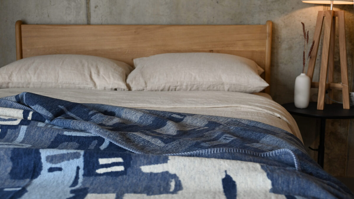 Blue abstract throw draped over stone linen on an oak bed.