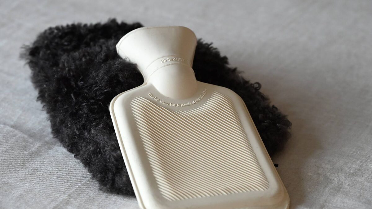 Mini hot water bottle laying on its dark brown faux fur cover.