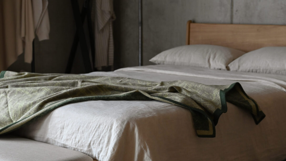 Green throw with crosshatch pattern and dark border spread over a neatly made bed.