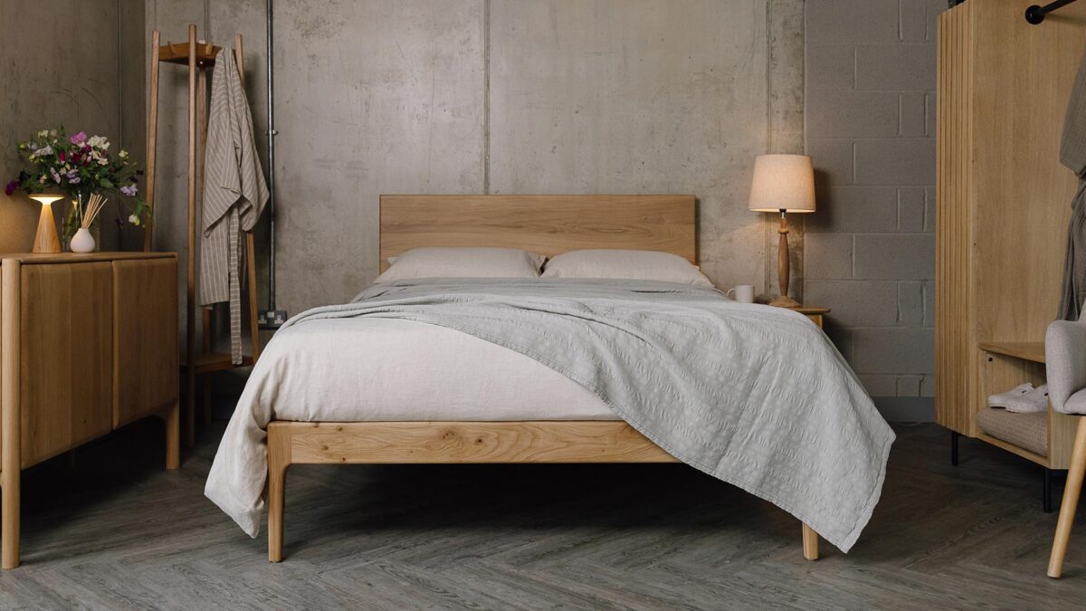 A forward facing shot of the English oak Chiswick, dressed in the organic linen bedding in ecru. The bedding is mostly covered up by a embroidered striped bedspread in the colour silver-grey, which also overhangs the bottom right-hand corner of the bed base.