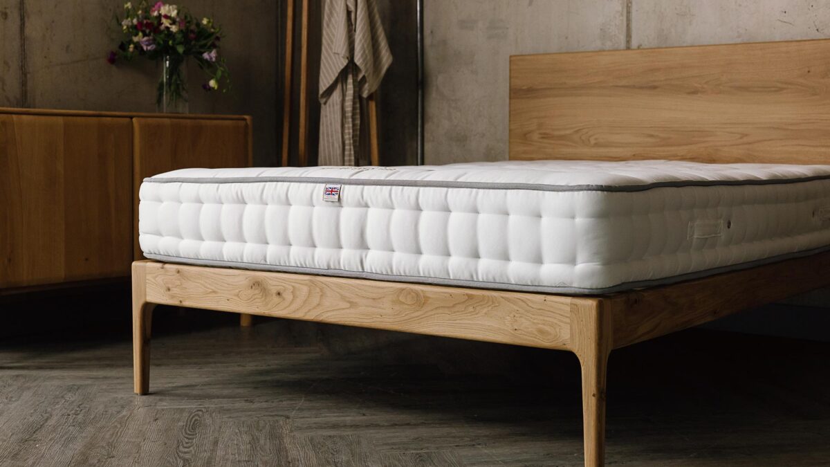 A low angled shot of the English oak Chiswick, focusing on the foot-rail/leg section of the bed base. The bed has bare mattress sat on it.