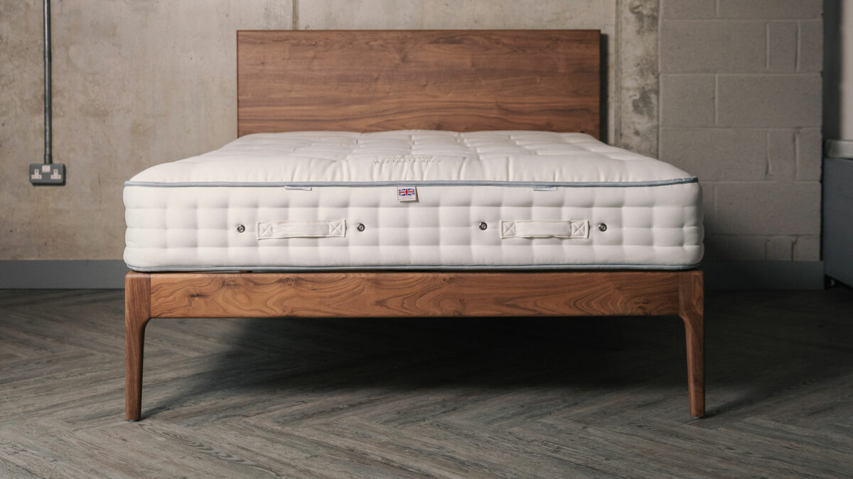 a view of a walnut wood Chiswick bed with mattress and without bedding