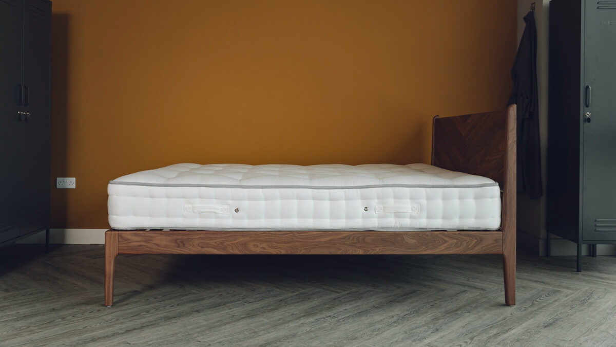 a solid walnut wood Hoxton bed with chevron pattern headboard shown from the side and without bedding