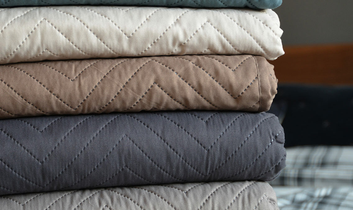 Chevron pattern lightly quilted bedspreads stacked and in a range of colours