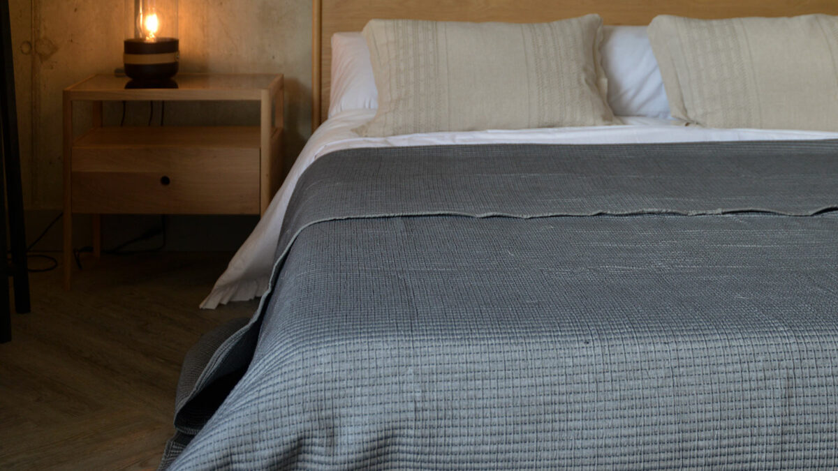 A steel-grey stitched bedspread is shown on our low solid Oak Carnaby bed.