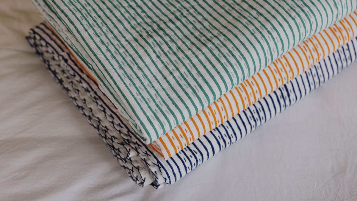 close up of blue, orange and green bedspreads stacked in a neat pile.