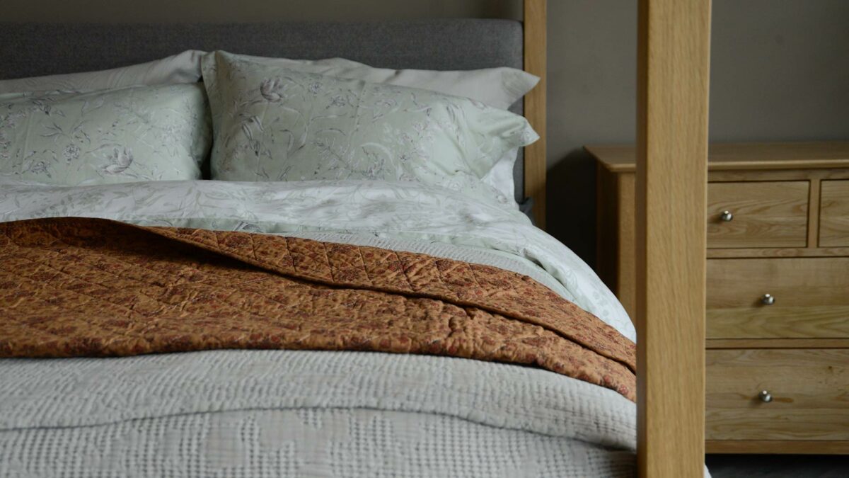 muted terracotta shades floral quilted throw shown on an oak bed