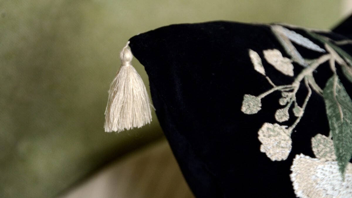 detail view of the corner tassel of the floral embroidered black velvet cushion