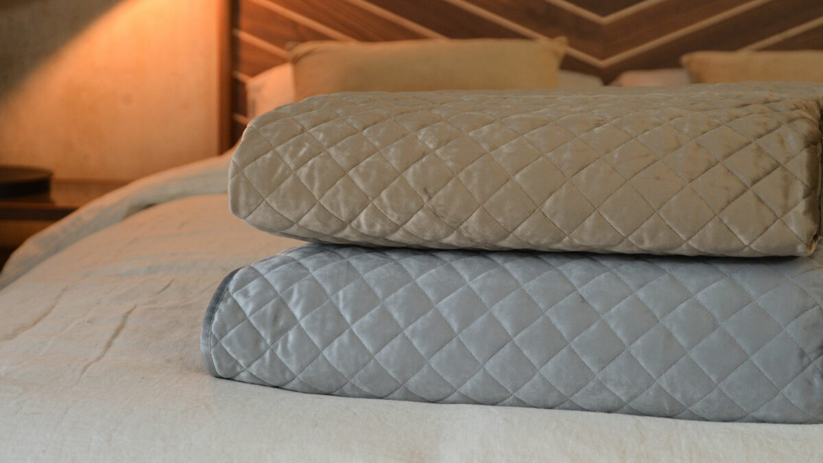 Taupe and silver grey coloured velvet-look quilted and reversible bedspreads shown together