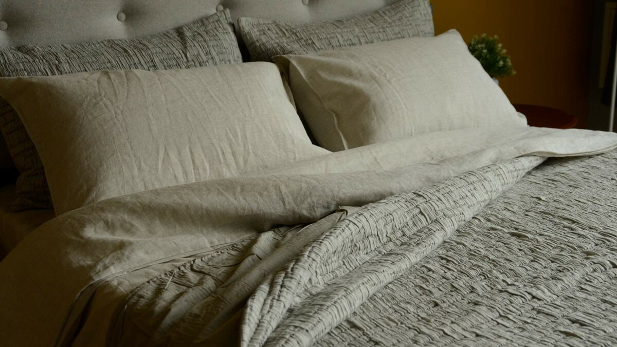 lightly quilted and textured crinkle effect bedspreads in warm grey shown on a kingsize bed